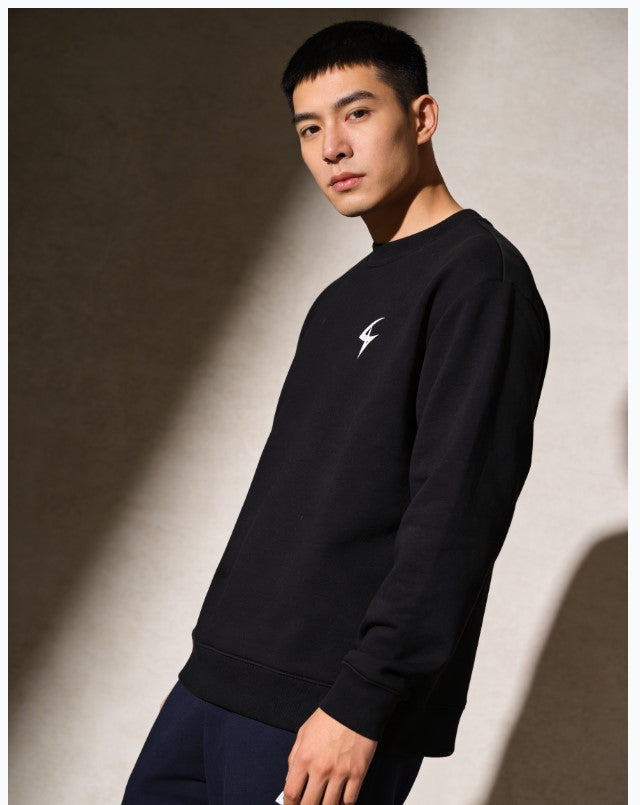 Man wearing a black sweatshirt with a logo against a neutral background
